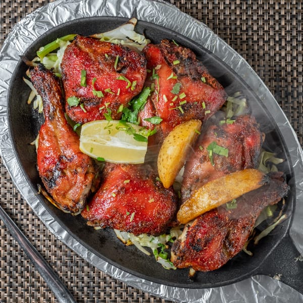 Steaming Indian Tandoori chicken with lemon and potato wedges in a hot skillet.