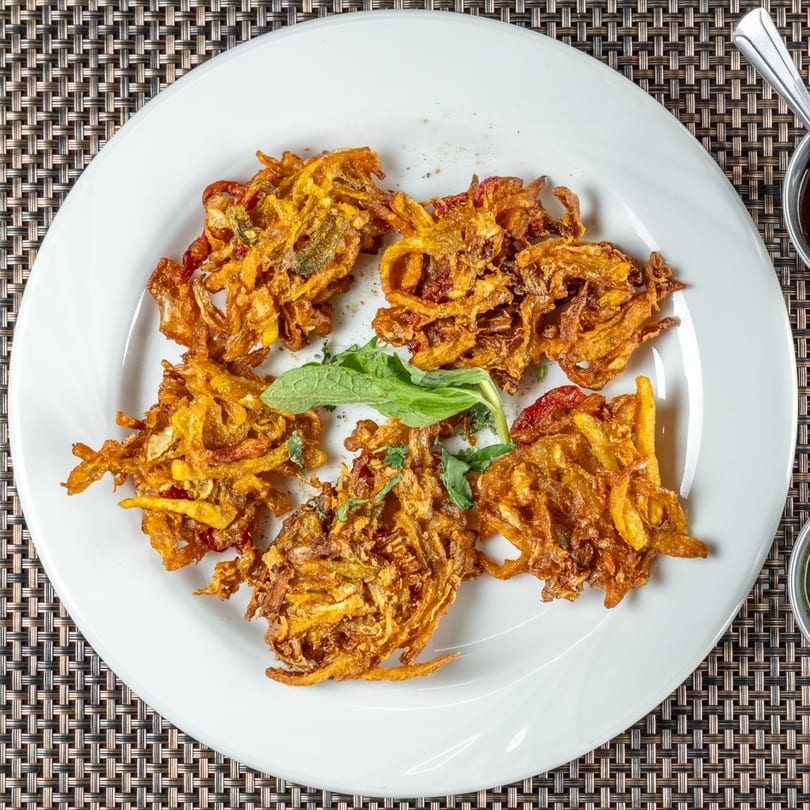 Five golden-brown Indian onion bhaji fritters with a sprig of mint on a white plate.