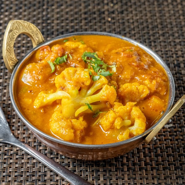 Aloo Gobi, an Indian dish with cauliflower and potatoes in a rich, orange sauce, garnished with cilantro.