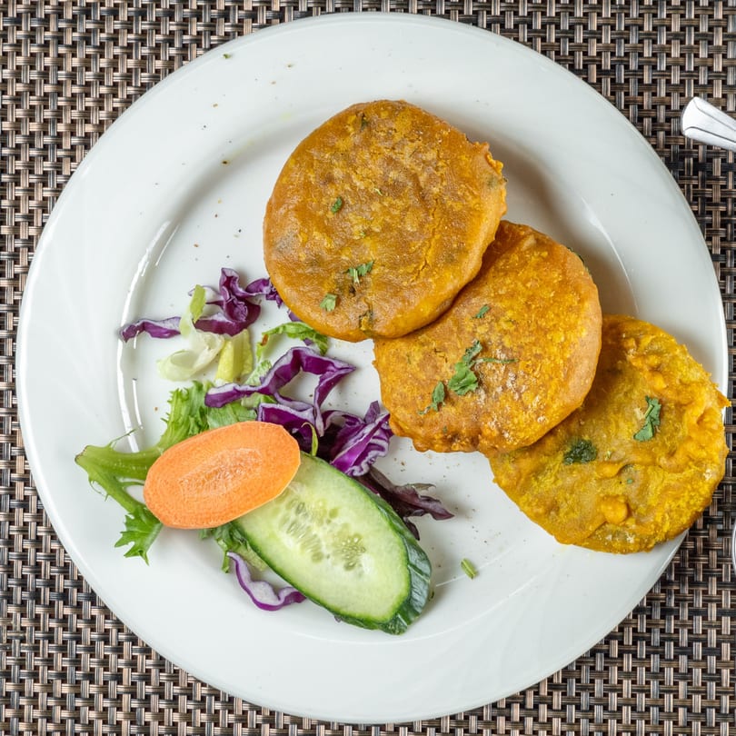 Three golden-brown Indian patties with fresh green and purple salad on a white plate.