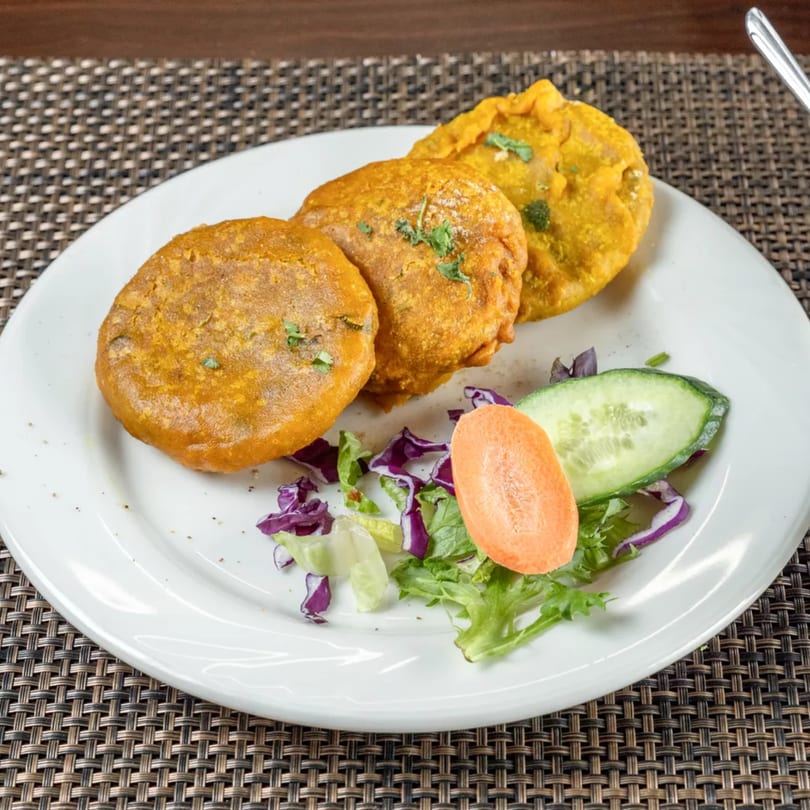 Three golden-brown Indian pakoras garnished with cilantro, served with a side salad on a white plate.