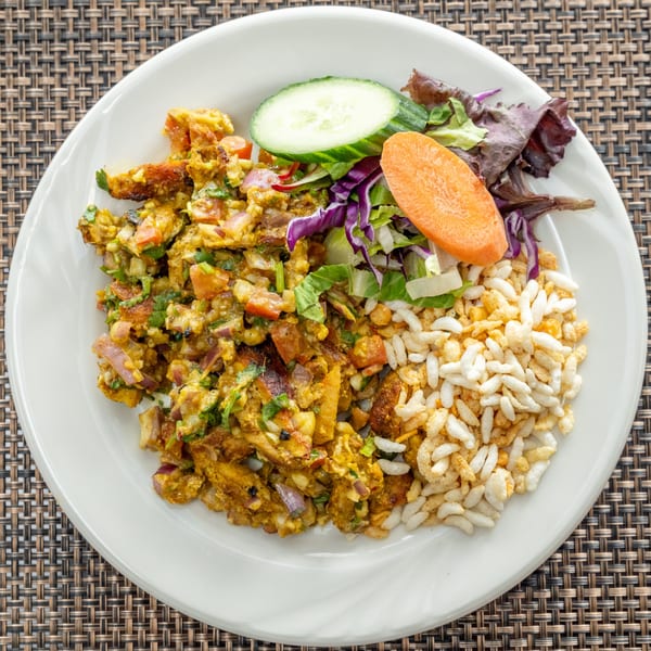 A plate of Indian bhel puri with salad, cucumber, and carrot on a woven placemat.