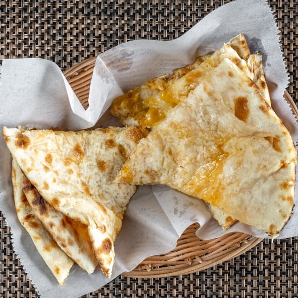 Golden brown Indian naan bread, some with melted cheese, served in a woven basket with parchment paper.