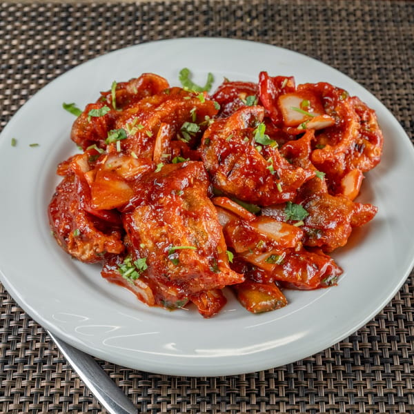 Chulo Cuisine's Indian chili chicken, a vibrant red dish garnished with fresh herbs on a white plate.