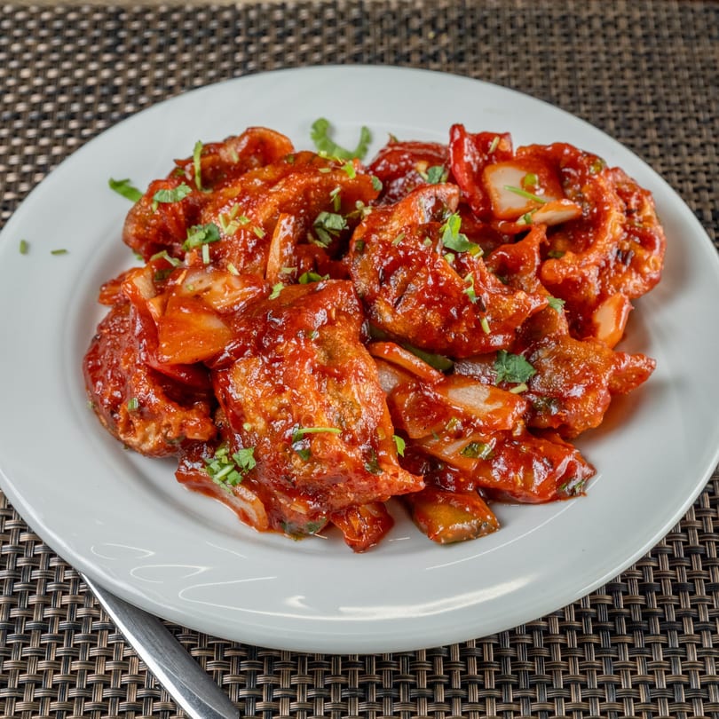 Chulo Cuisine's Indian chili chicken, a vibrant red dish garnished with fresh herbs on a white plate.