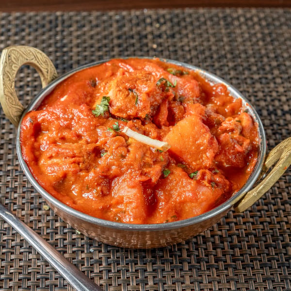 A close-up of Indian chicken tikka masala in a traditional copper bowl on a woven placemat.
