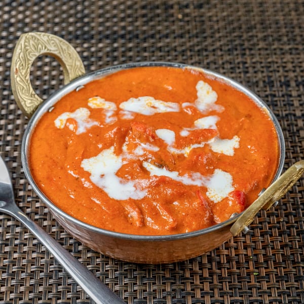 Indian butter chicken, a creamy orange curry with white swirls, in a decorative copper bowl.