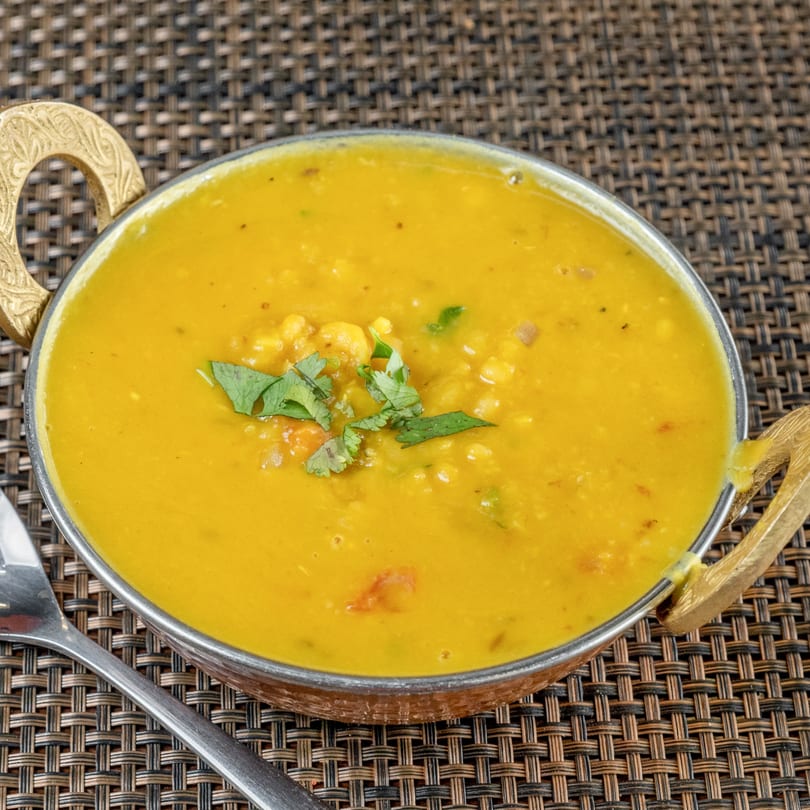 A golden Indian lentil dal, garnished with fresh cilantro, in a decorative metal bowl.